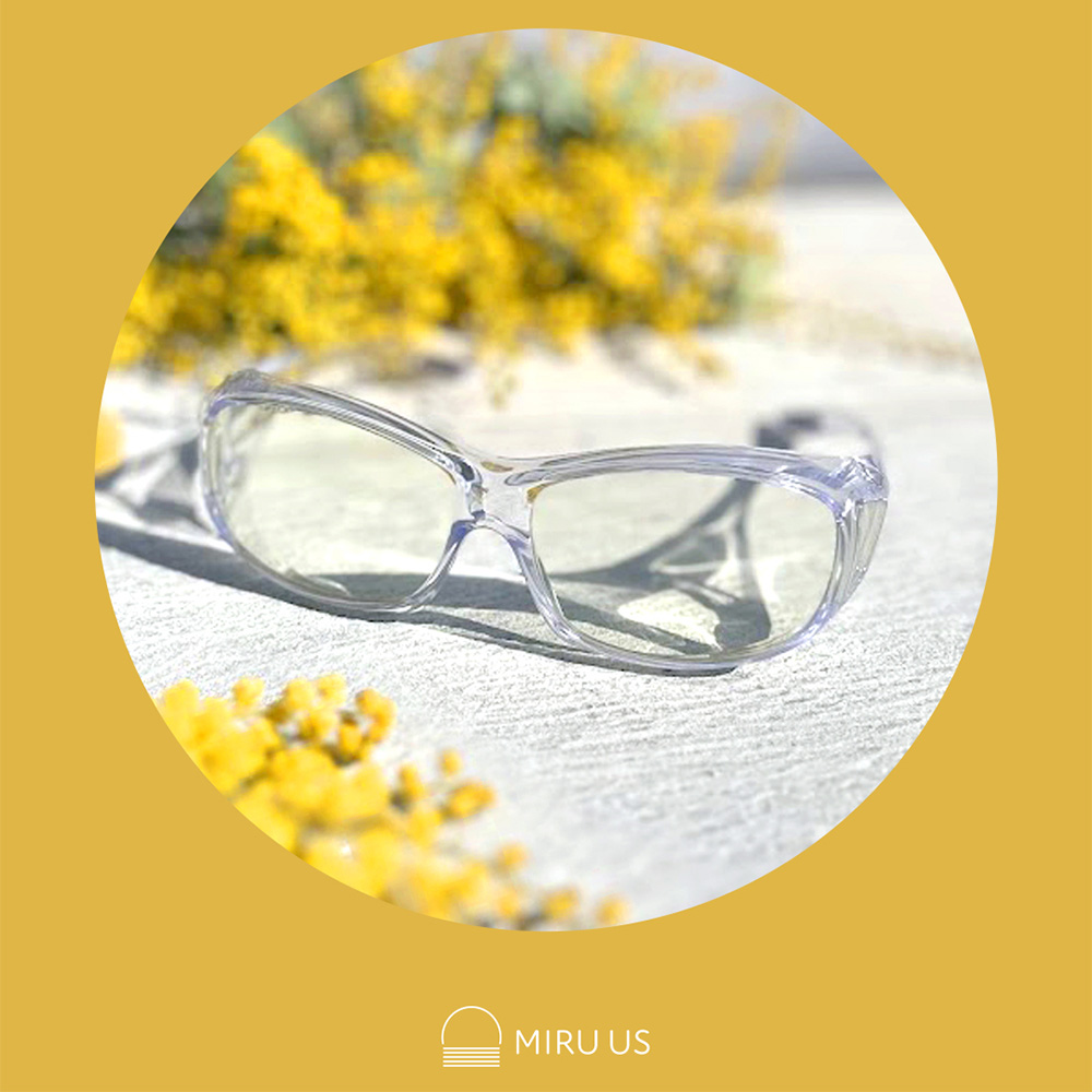 ミモザの花を背景にしたクリアフレームの花粉対策メガネ「アイシェルター」の商品イメージ。