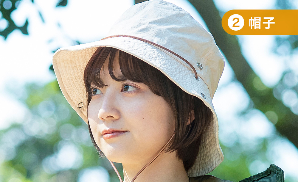 つばの広い帽子をかぶり、斜め上を見つめる女性。上からの花粉を防ぐ外出イメージ。