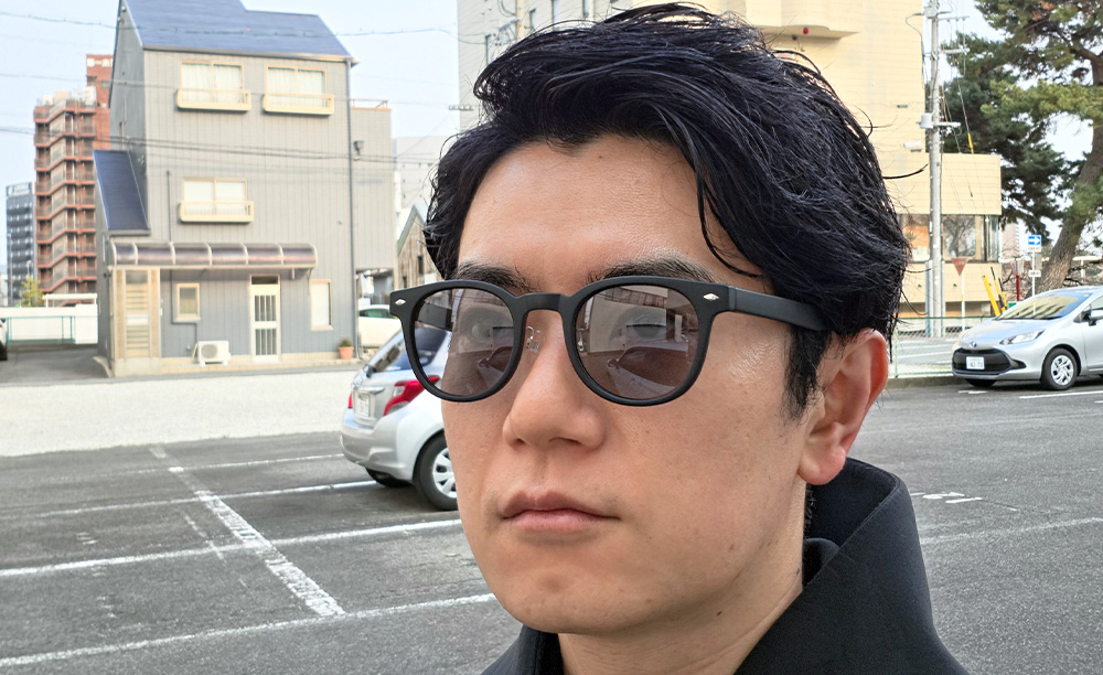 晴天の屋外でグレーレンズが自然に色づいた偏光調光グラスの装着イメージ。目元が見える程度の濃