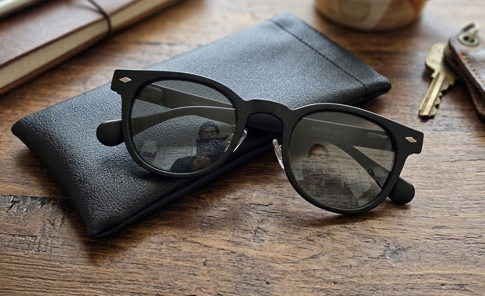 木のテーブルに置かれたマットブラックフレームの偏光調光グラスと専用ケース