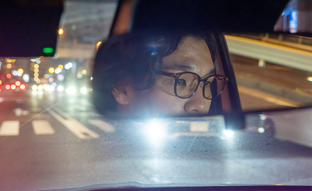 夜間の運転中に感じる対向車のLEDヘッドライトの眩しさと、それによる視界不良に悩むドライバーの様子。
