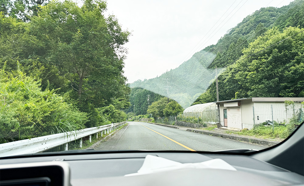 夏のドライブ中の運転席からの視界。フロントガラスにダッシュボードの映り込みが発生し、路面の照り返しによって白線や前方の状況が確認しにくくなっている様子。